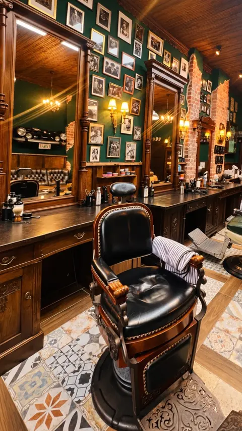 Ein schwarzer Barberstuhl aus Leder vor der Spiegelreihe und der grünen Wand voller gerahmter Porträts